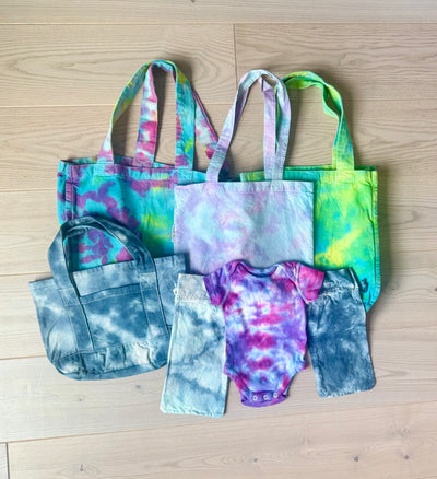Collection of tie-dye baby items including bags, shorts, and a onesie from Arts & Crafted