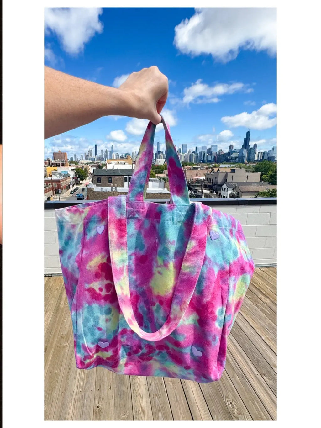 Colorful tie-dye bag held by a hand with a city skyline in the background