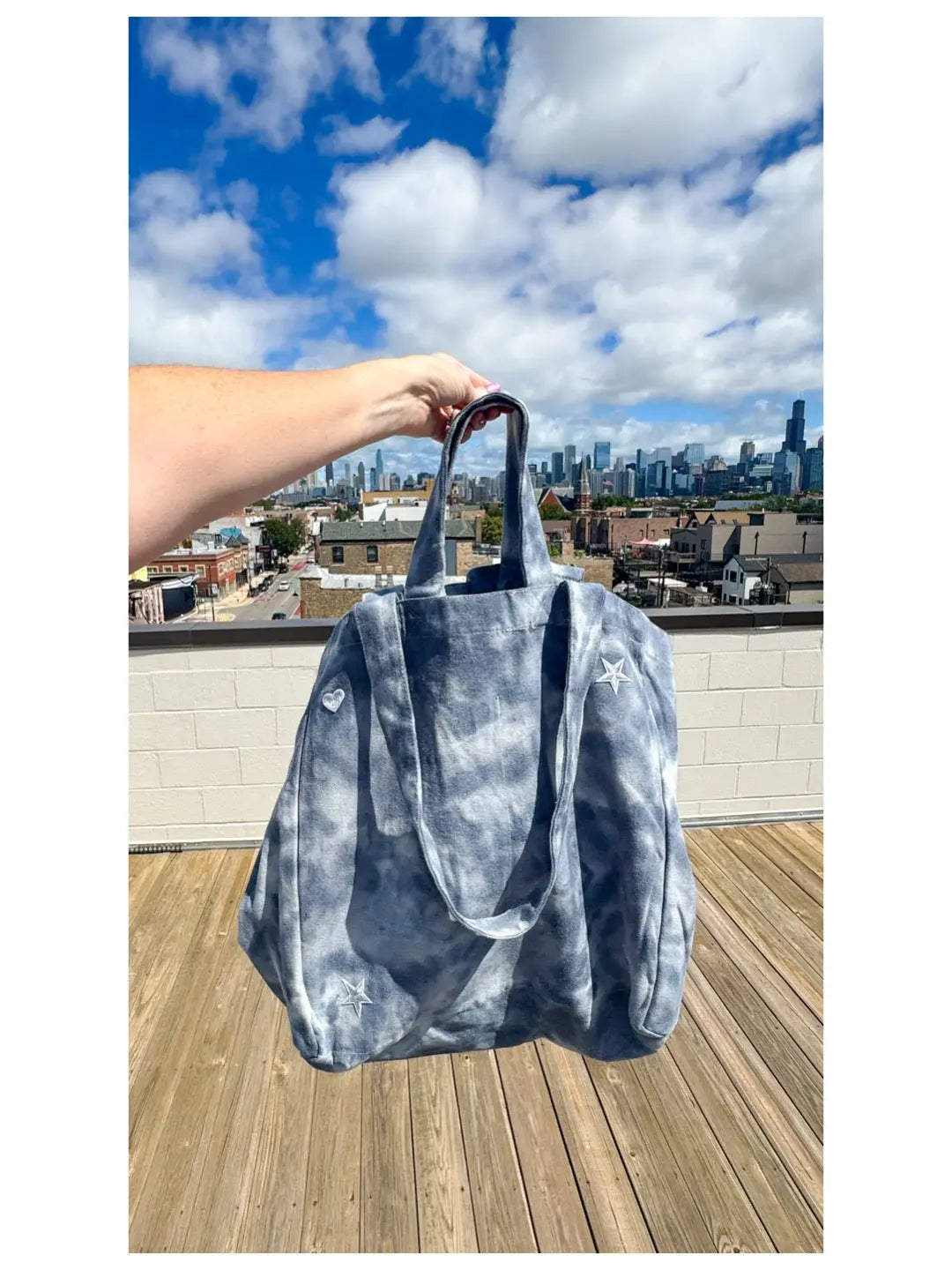 Person holding a blue tie-dye bag on a rooftop with a city skyline in the background